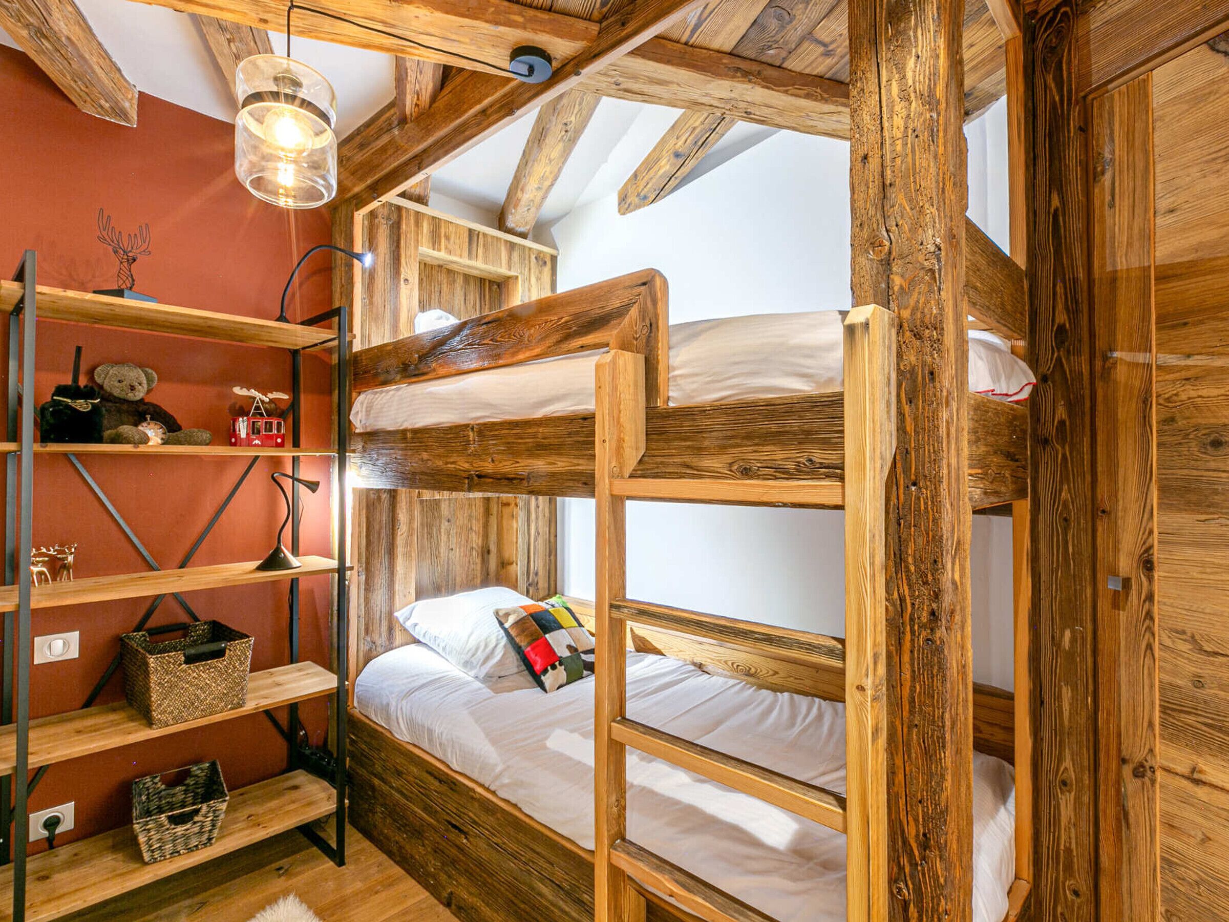A rustic room with wooden bunk beds, shelves with various items, and a hanging light fixture.