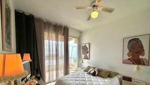 A hotel room with a bed, a desk, a chair, a ceiling fan, and a window with curtains.