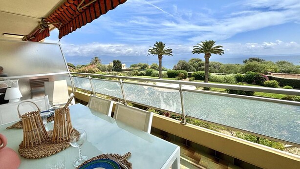 A balcony with a glass table, a view of a river, and palm trees.