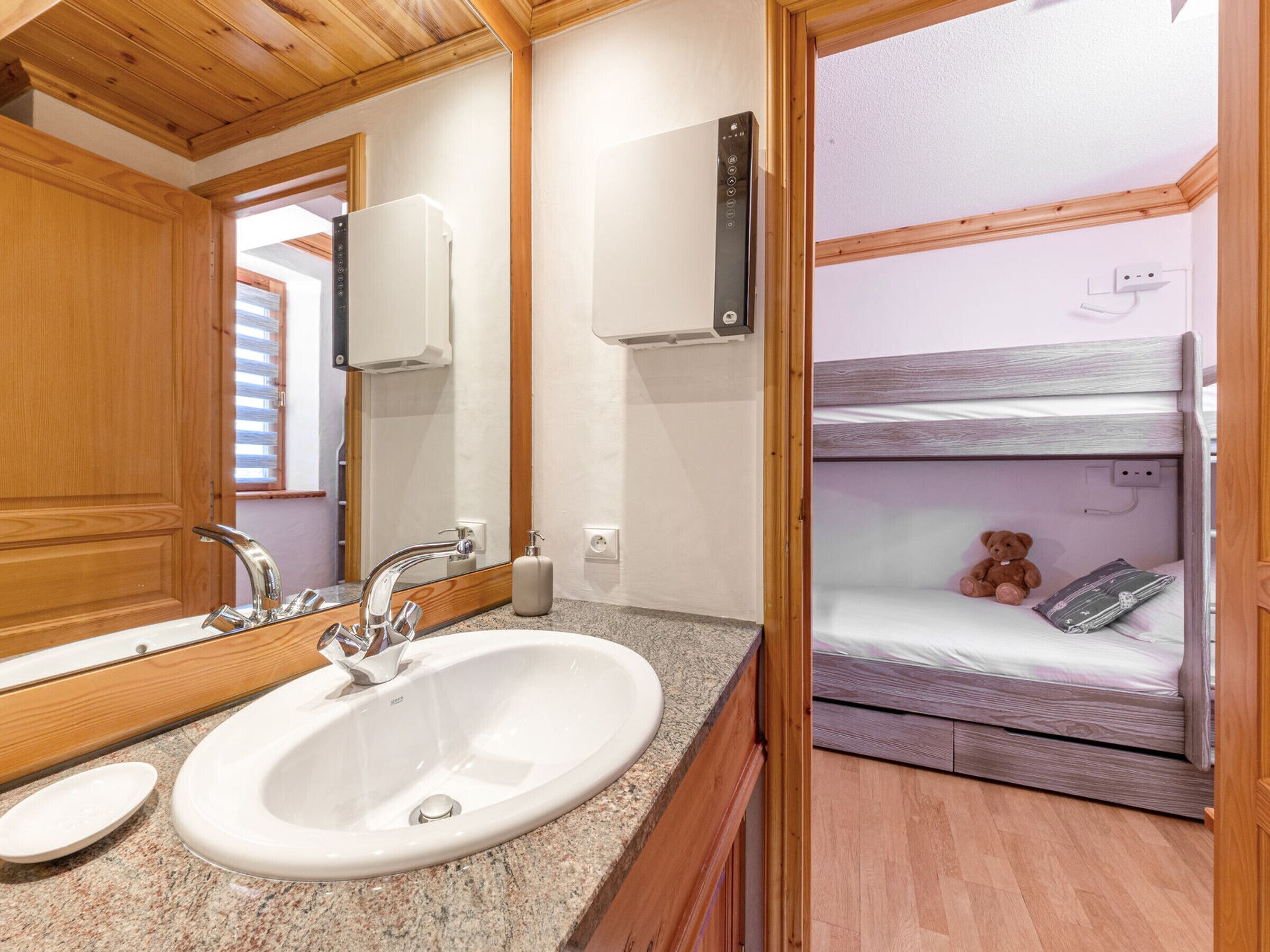 A bathroom with a sink, mirror, and a bunk bed in the adjacent room.