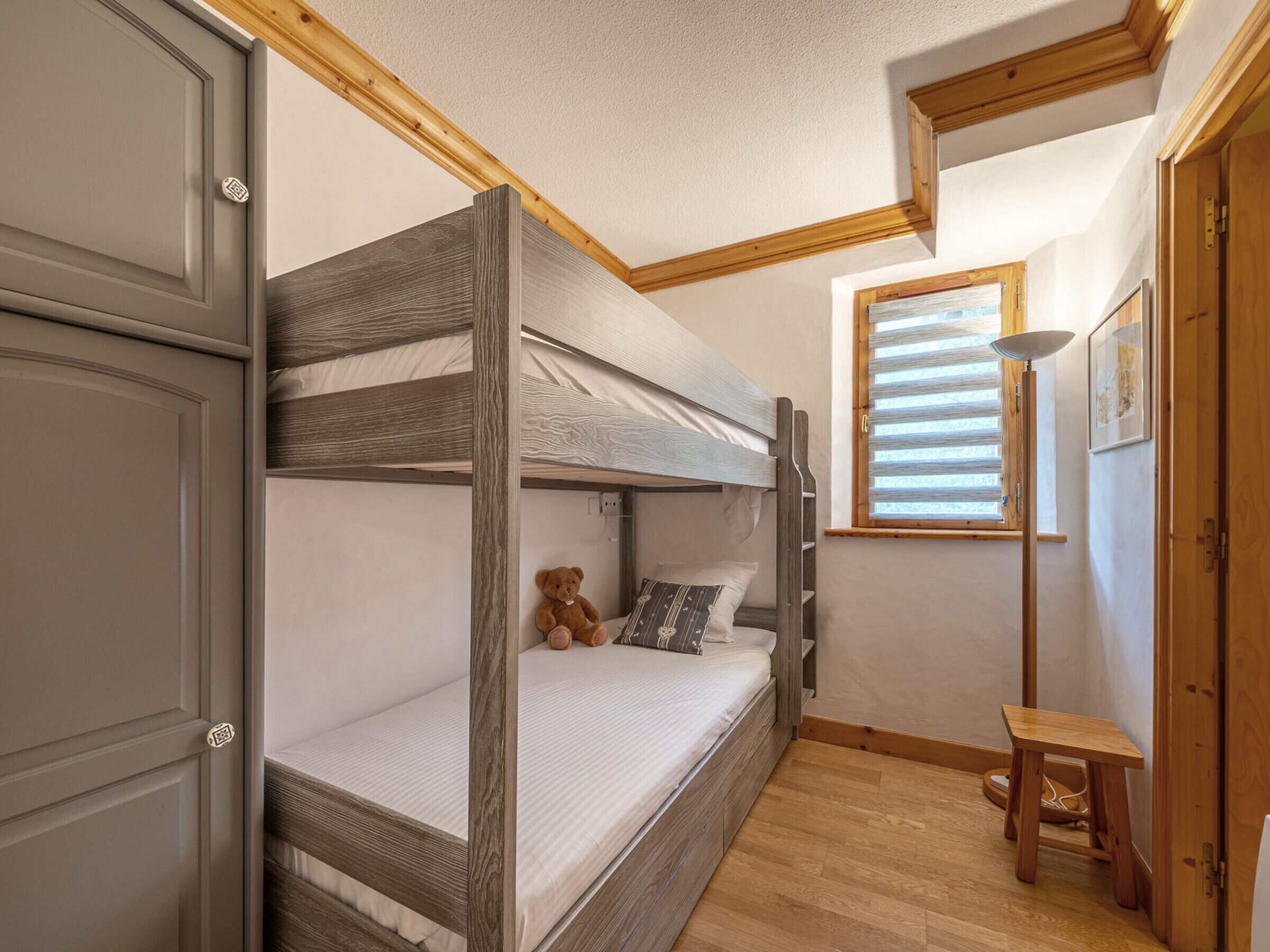 A bunk bed room with a wooden headboard, a small table, and a window with blinds.