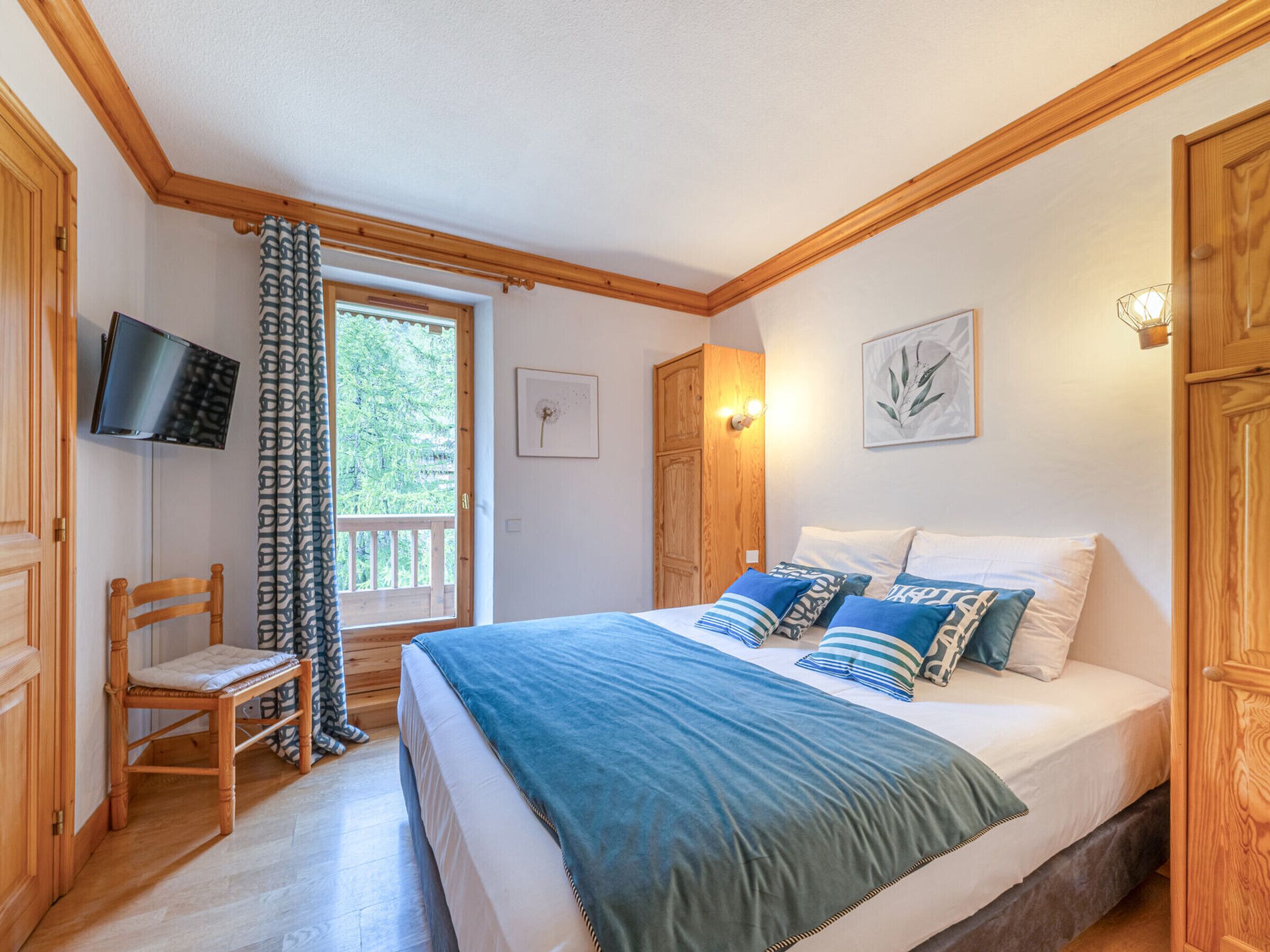 Ein Schlafzimmer mit einem Bett, einem Sessel, einem Fernseher und einem Fenster mit Vorhängen.