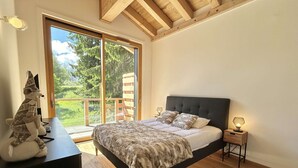 Un dormitorio con una cama grande, un escritorio de madera y vistas al exterior a través de un ventanal corredero.