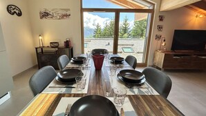 Un comedor con una mesa grande dispuesta para seis personas, un televisor y vistas al exterior.