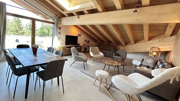 Un loft espacioso con techos altos, vigas de madera, una zona de comedor con mesa y sillas, un sofá y un televisor.