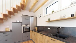 Eine moderne Küche mit grauen Schränken, einer Holztreppe, einem schwarzen Spülbecken und einem Fenster mit einer Uhr.