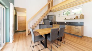 Eine moderne Küche mit Holzausstattung, ein Essbereich mit Holztisch und Stühlen sowie eine Treppe zu einer oberen Ebene.