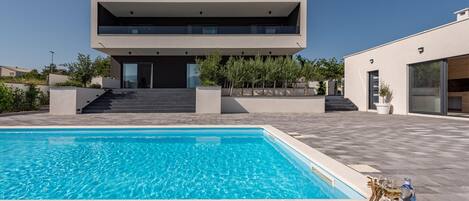 A modern house with a swimming pool, a staircase leading to the entrance, and a patio area with lounge chairs.