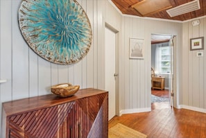 A hallway with wooden flooring, a decorative wall piece, and a wooden console table with a bowl. - Oak Grove Cottage at Fernandina Beach (Fernandina Beach)