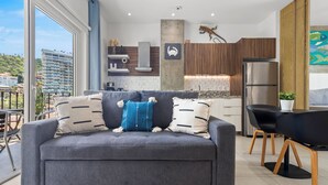 A modern living room with a grey sofa, a dining table with black chairs, and a kitchen area in the background. - Cozy Retreat in Romantic Zone - Gym & BBQ (Puerto Vallarta)