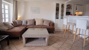A living room with a brown sectional sofa, a checkered coffee table, and a kitchen area with white cabinets and bar stools. - Duplexe with panoramic south-facing terrace in the center of Grimaud (Grimaud)