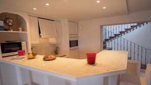 A modern kitchen with white cabinetry, a central island, and a staircase leading to an upper floor. - Duplexe with panoramic south-facing terrace in the center of Grimaud (Grimaud)