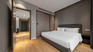 A modern bedroom with a large bed, a walk-in closet, and a hallway leading to another room.