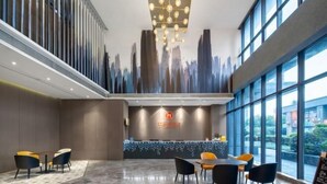 A modern hotel lobby with a reception desk, seating area, and large windows offering a view of the cityscape. - Huanlesong Hotel (Jiaxing Zhongguancun Wanli Square) (Jiaxing)