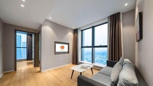 A modern living room with a sofa, a coffee table, and a large window offering a city view. - Huanlesong Hotel (Jiaxing Zhongguancun Wanli Square) (Jiaxing)