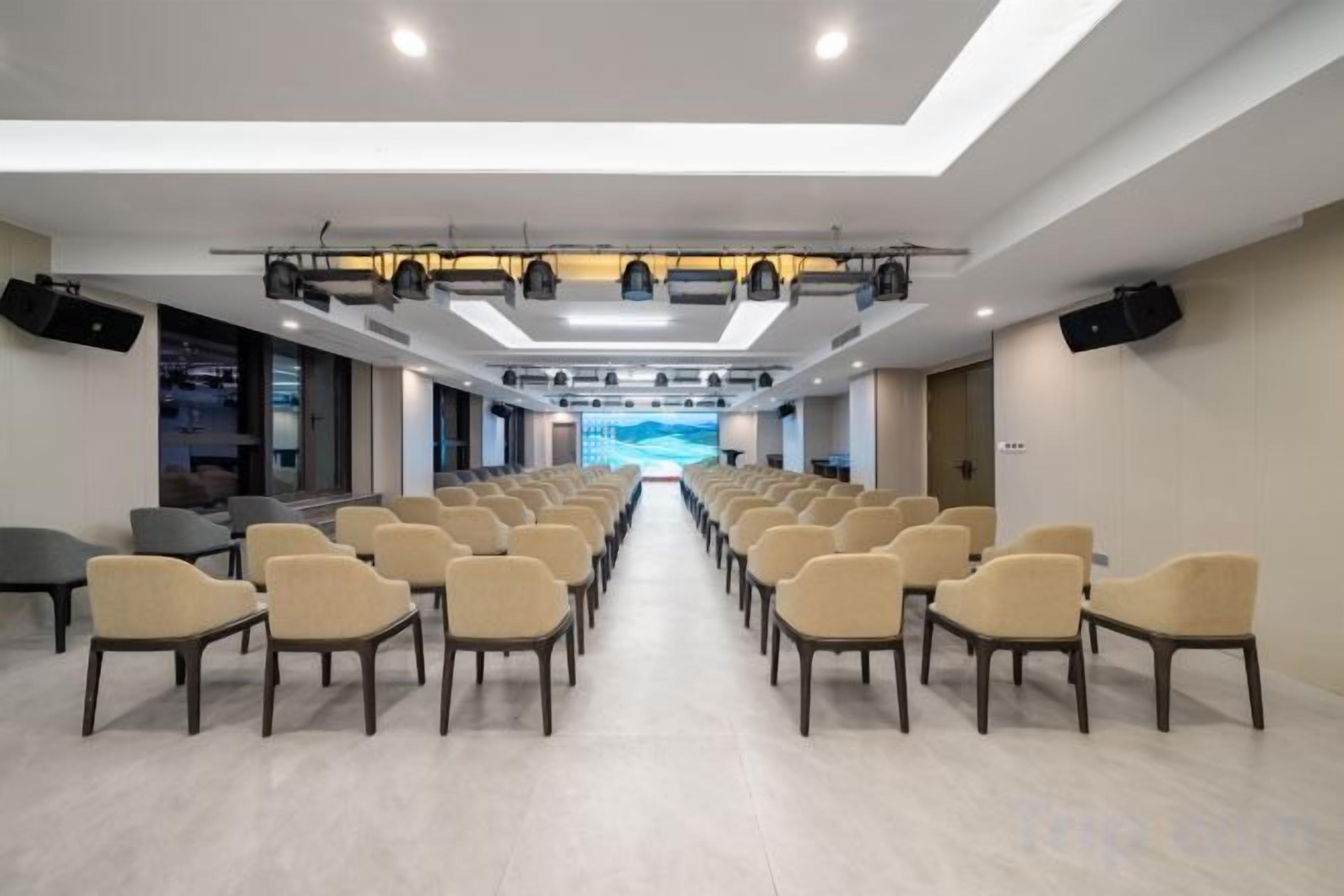 Un salón de conferencias con filas de sillas orientadas hacia un escenario, equipado con sistemas de iluminación y sonido.