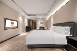 Habitación de hotel con una cama grande, un escritorio, una silla y un televisor en la pared.