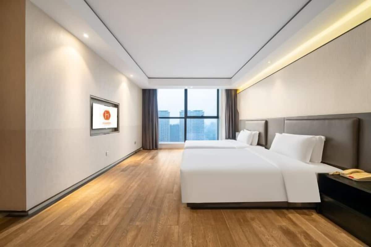 A hotel room with a large bed, a bedside table, a window with a city view, and a framed picture on the wall.