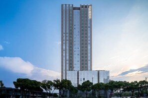 Un edificio alto y moderno con fachada de vidrio, rodeado de árboles y otros edificios.