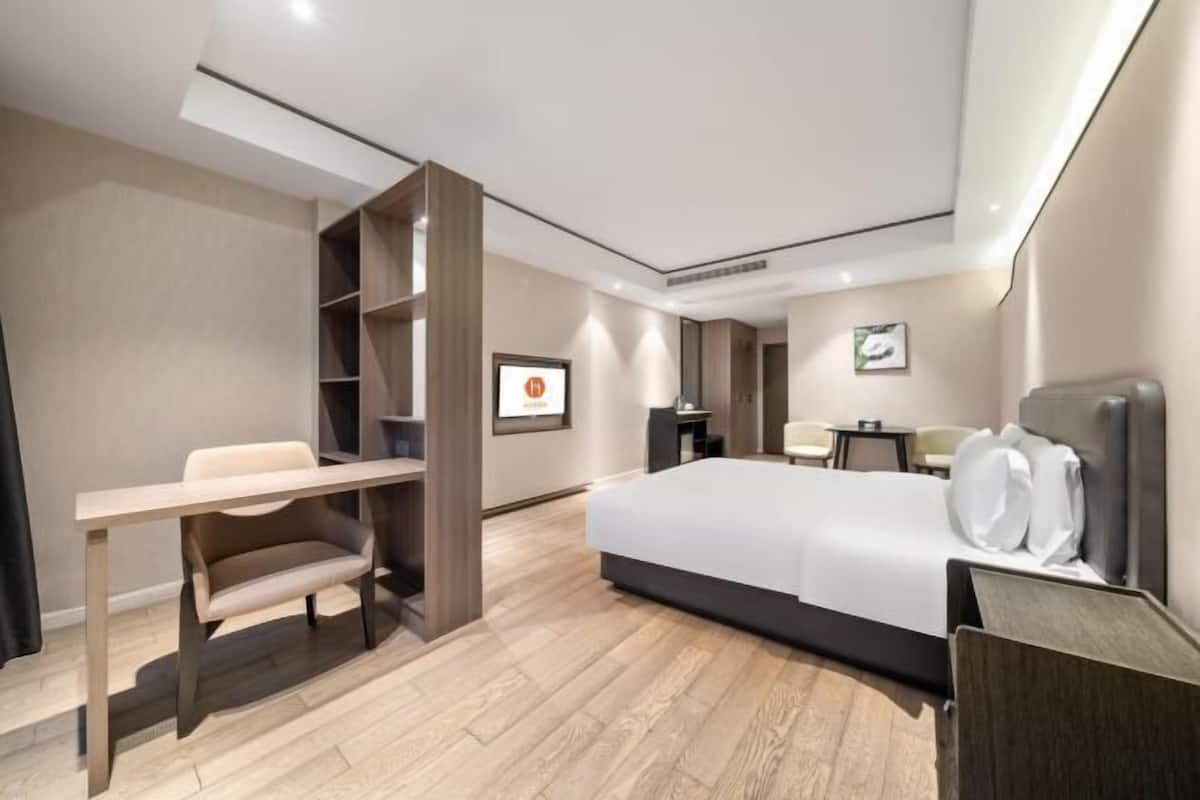 A modern hotel room with a bed, desk, chair, and a small table.