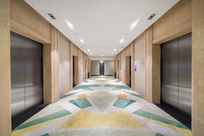 Pasillo de hotel con piso alfombrado, paredes de madera y ascensores a ambos lados.
