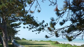 A wooden deck with stone railings overlooking a grassy area and the ocean. - Résidence de Tourisme Le Sherman (Colleville-sur-Mer)