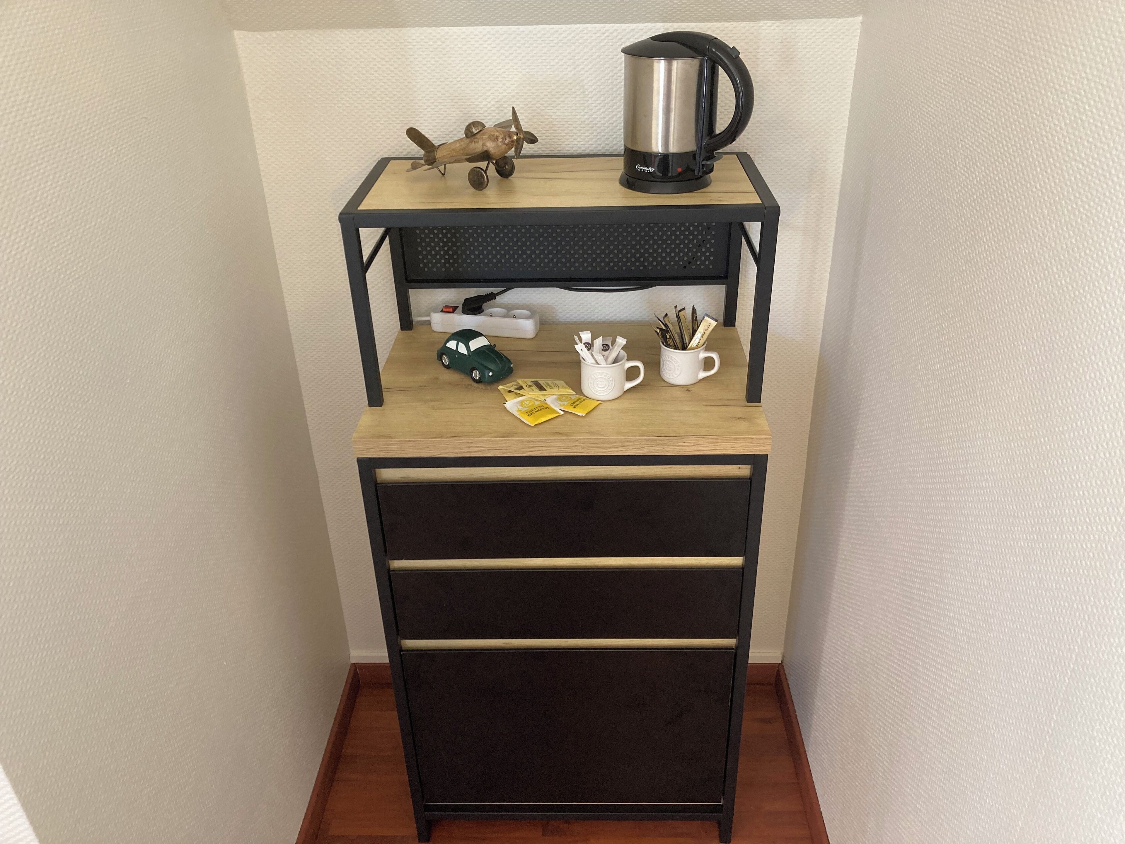 A small wooden desk with a black metal frame, a kettle, a toy car, and two mugs with pens.