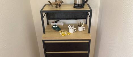 A small wooden desk with a black metal frame, a kettle, a toy car, and two mugs with pens.
