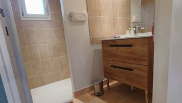 Ein Badezimmer mit beigen Fliesen, einem Holzkosmetikschrank, einem Spiegel und einem Fenster.