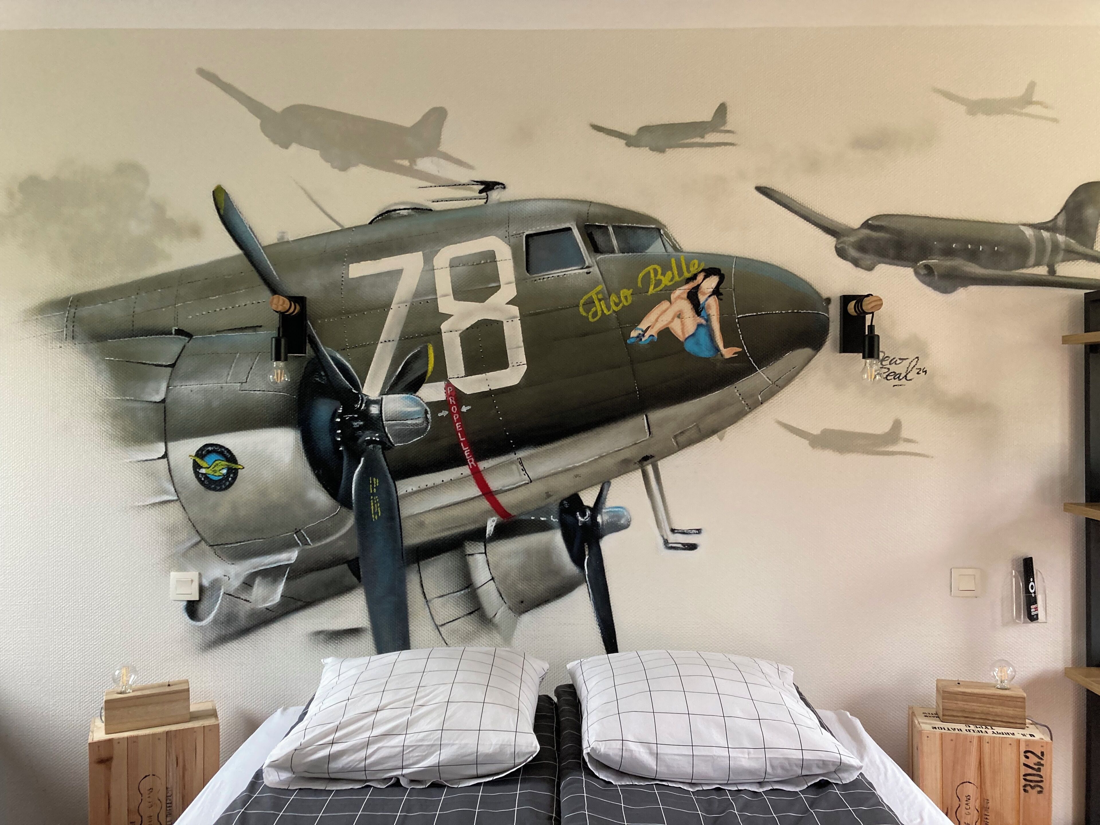 A bedroom with a mural of a military aircraft, a bed with a grid-patterned bedspread, and two wooden nightstands with decorative items.
