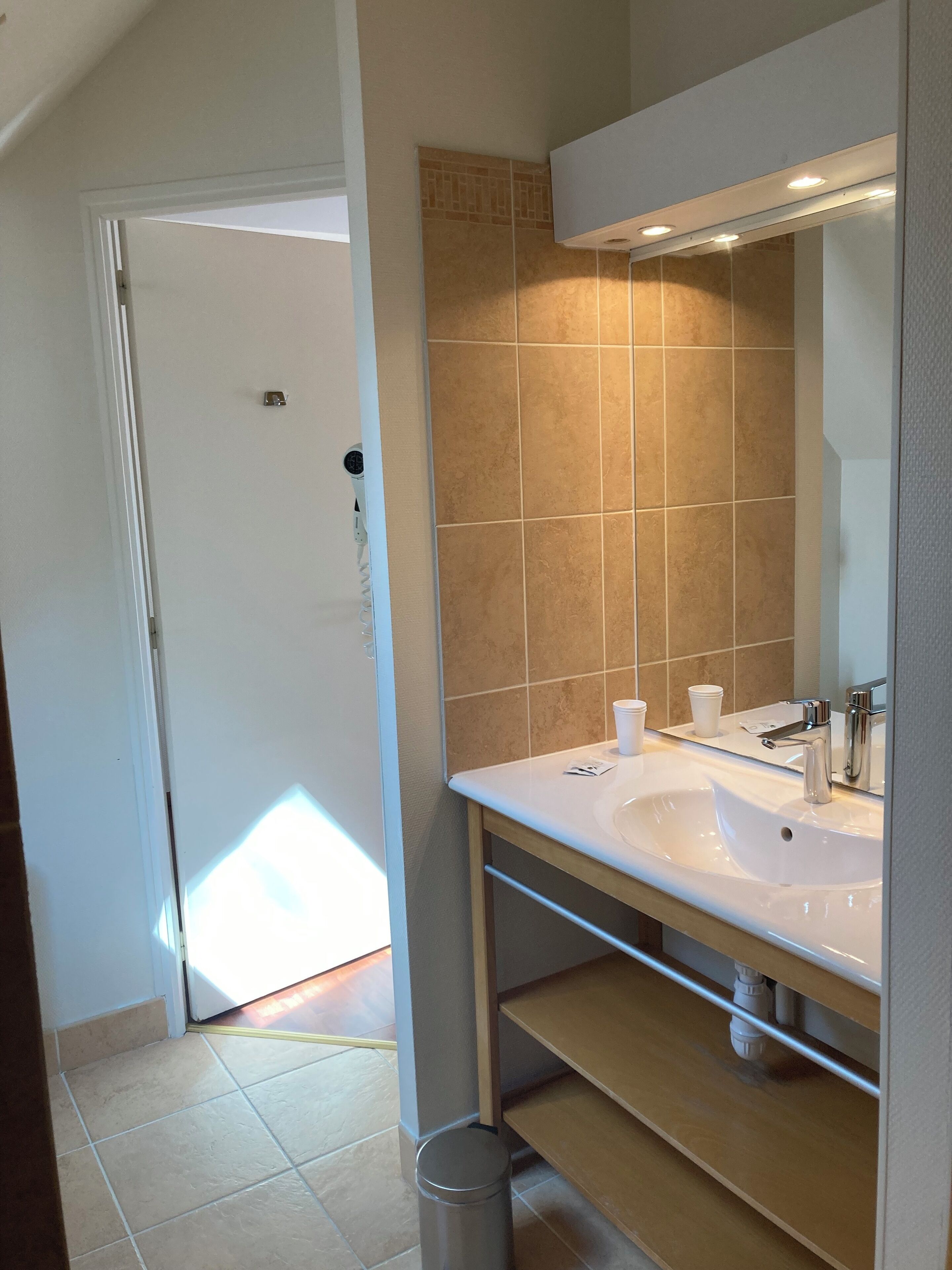 Baño con lavamanos blanco, un espejo y azulejos color beige.