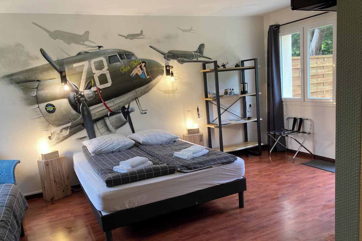 A bedroom with a bed, a wooden floor, a bookshelf, and a window.