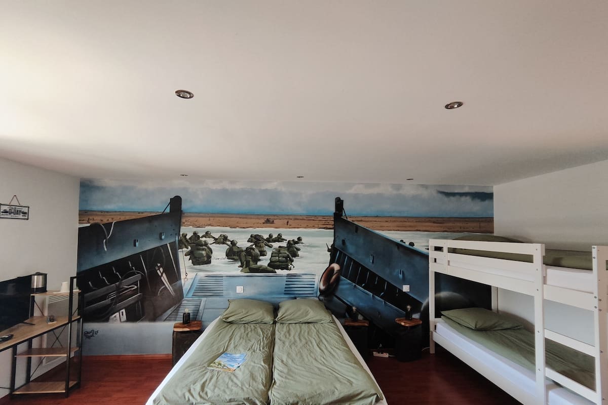 A room with bunk beds, a mural of soldiers on a beach, and a small desk with a lamp.