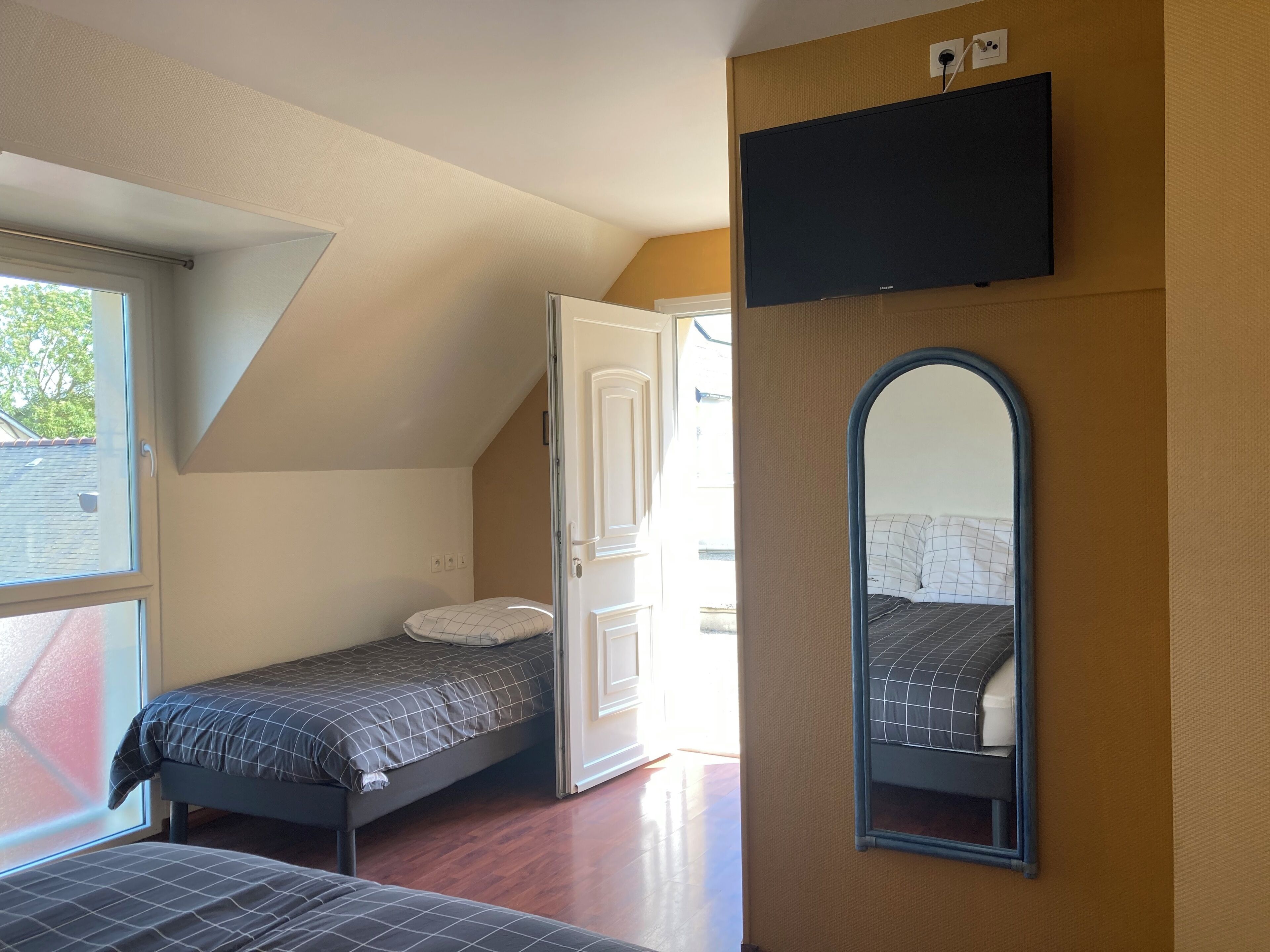 A bedroom with a loft bed, a small bedside table, a mirror, and a TV mounted on the wall.