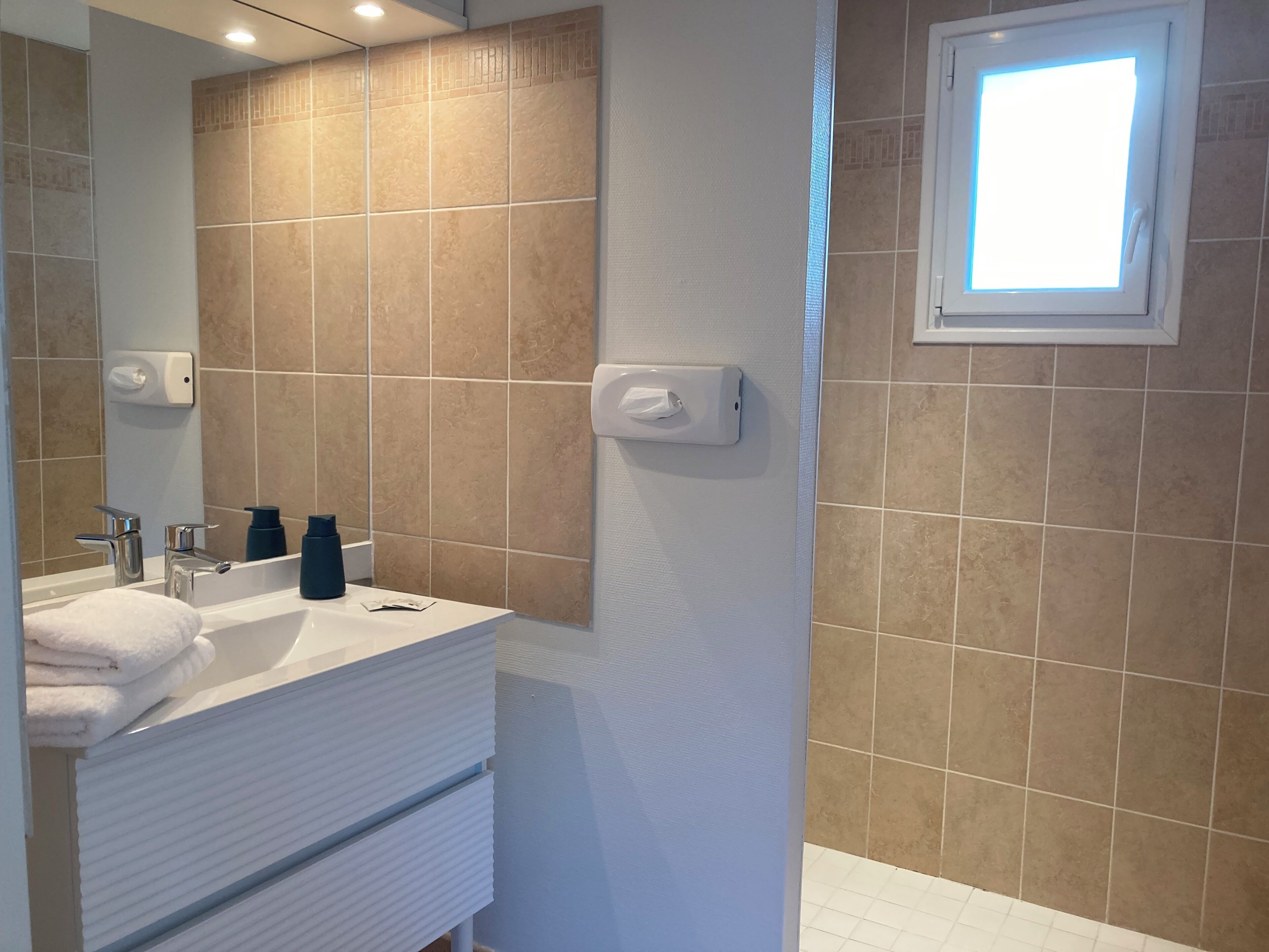 A modern bathroom with a white vanity, a large mirror, and a window with a view of the outside.