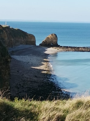 A coastal landscape with a rocky beach, a lighthouse, and a clear view of the sea. - Résidence de Tourisme Le Sherman (Colleville-sur-Mer)