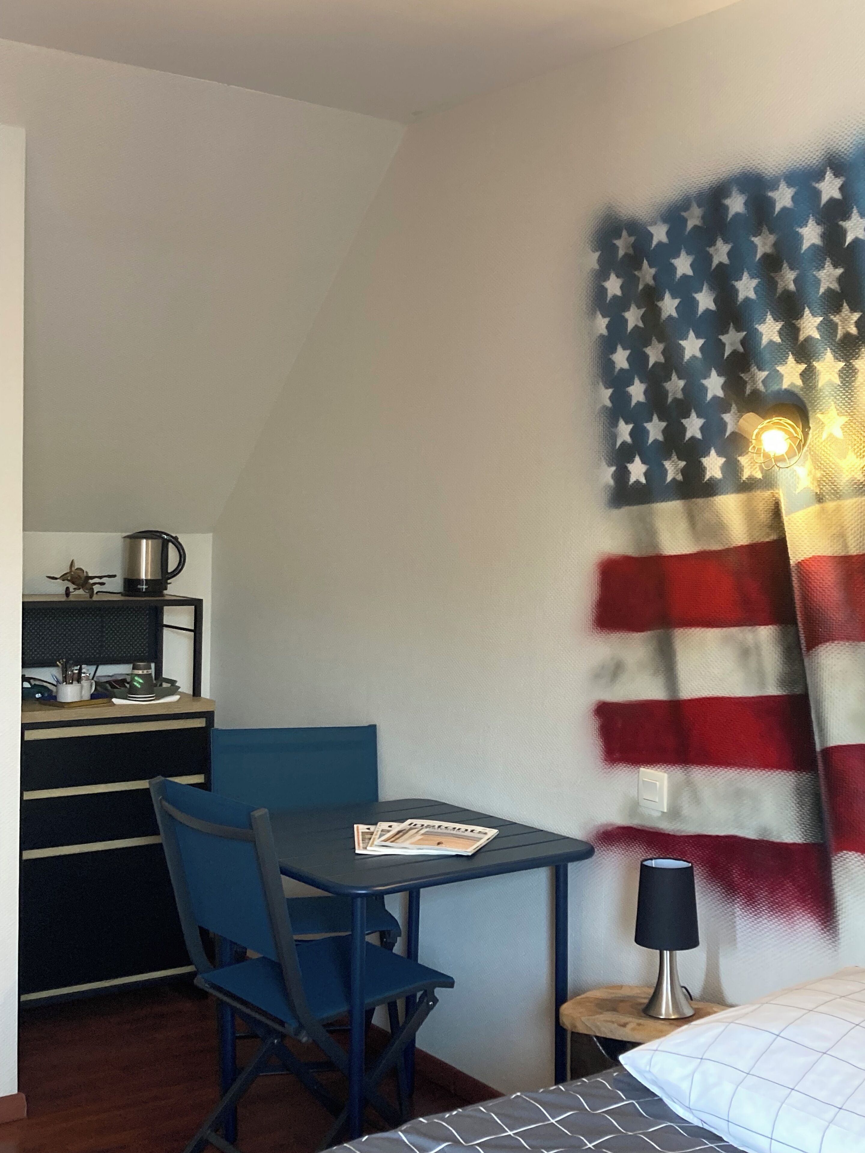 A room with a desk, chair, and a bed. There is a wall with an American flag design.