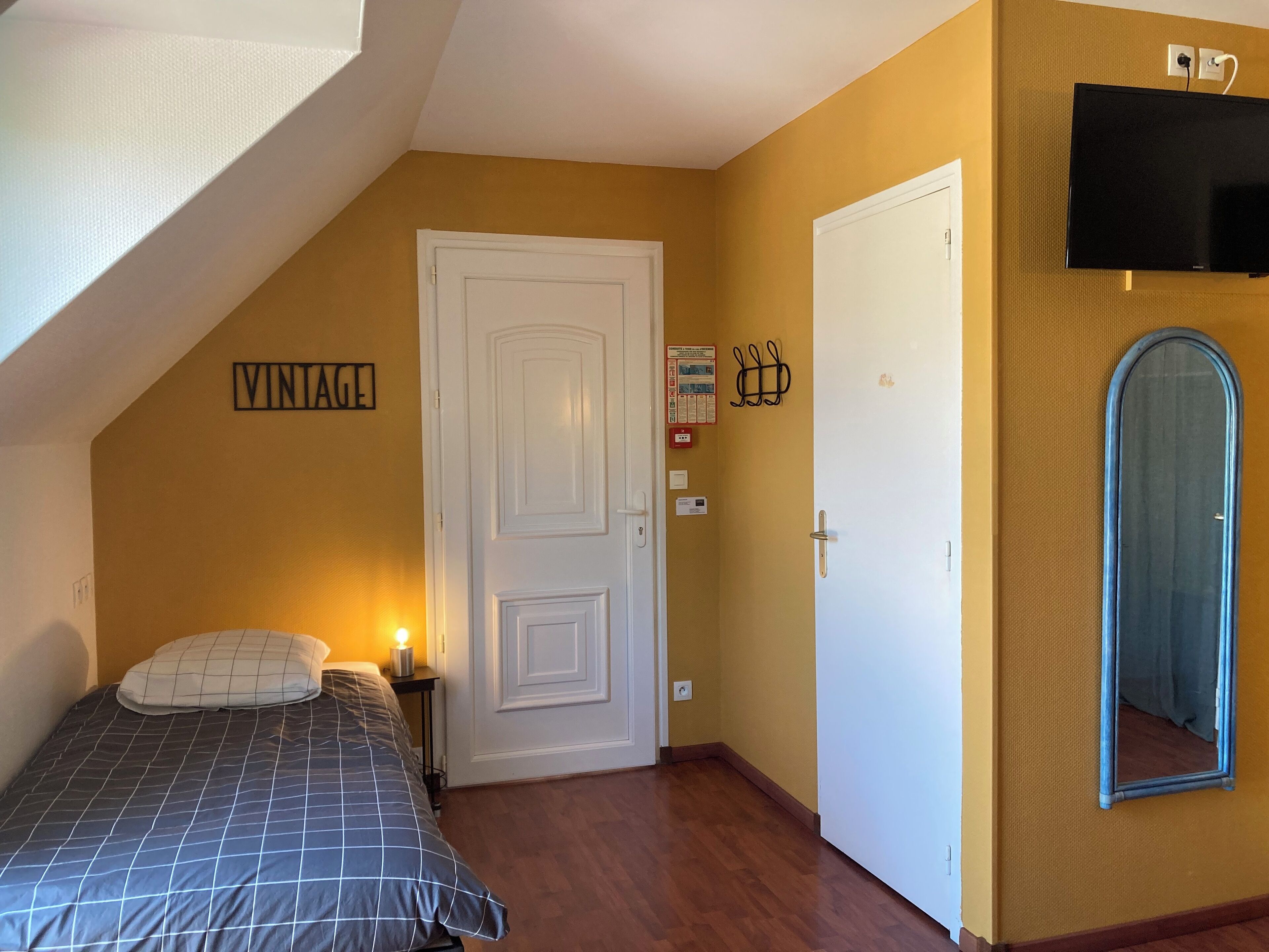 A bedroom with a bed, a white door, a mounted TV, and a mirror.
