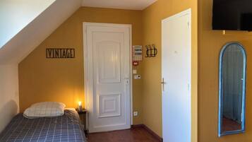 A bedroom with a bed, a white door, a mounted TV, and a mirror.