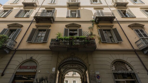 A building with multiple balconies, a storefront with a sign, and an archway entrance.