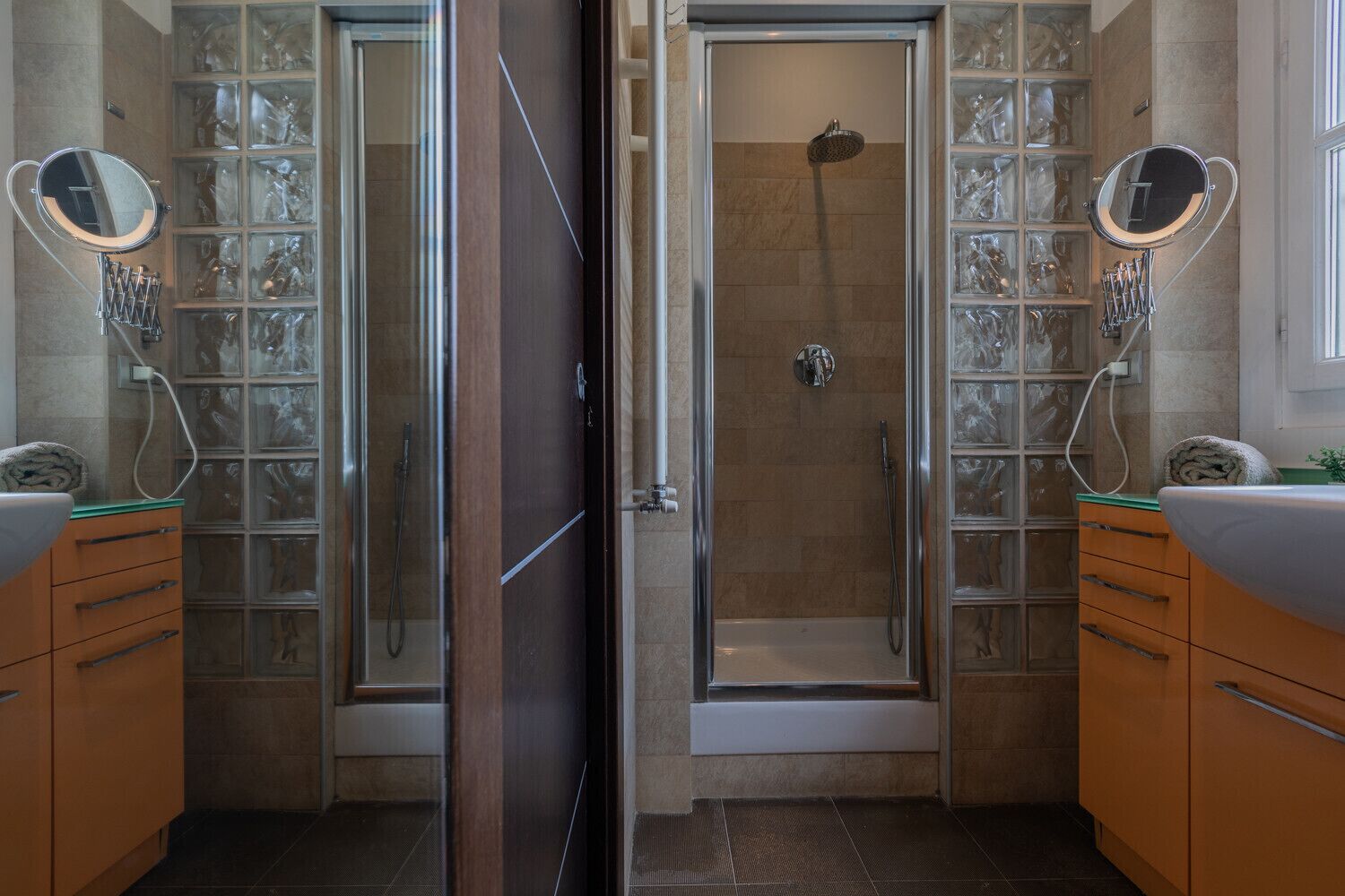 Ein modernes Badezimmer mit einer Duschkabine aus Glas, zwei Waschbecken und dekorativen Glasregalen.