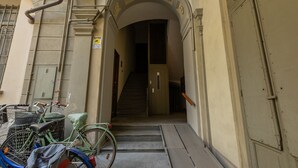 A narrow hallway with a staircase leading to a door, a bicycle parked on the left, and a sign indicating a left turn.
