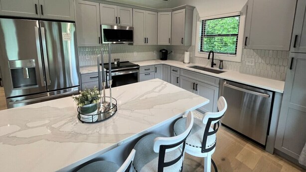 A modern kitchen with white cabinets, stainless steel appliances, and a marble island. - The Crepe Myrtle Cottage (Franklin)