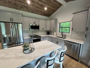 A modern kitchen with white cabinets, stainless steel appliances, and a marble island. - The Crepe Myrtle Cottage (Franklin)