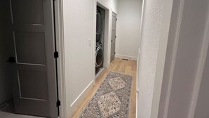 A narrow hallway with a washing machine in the background, a patterned rug on the floor, and white walls. - The Crepe Myrtle Cottage (Franklin)