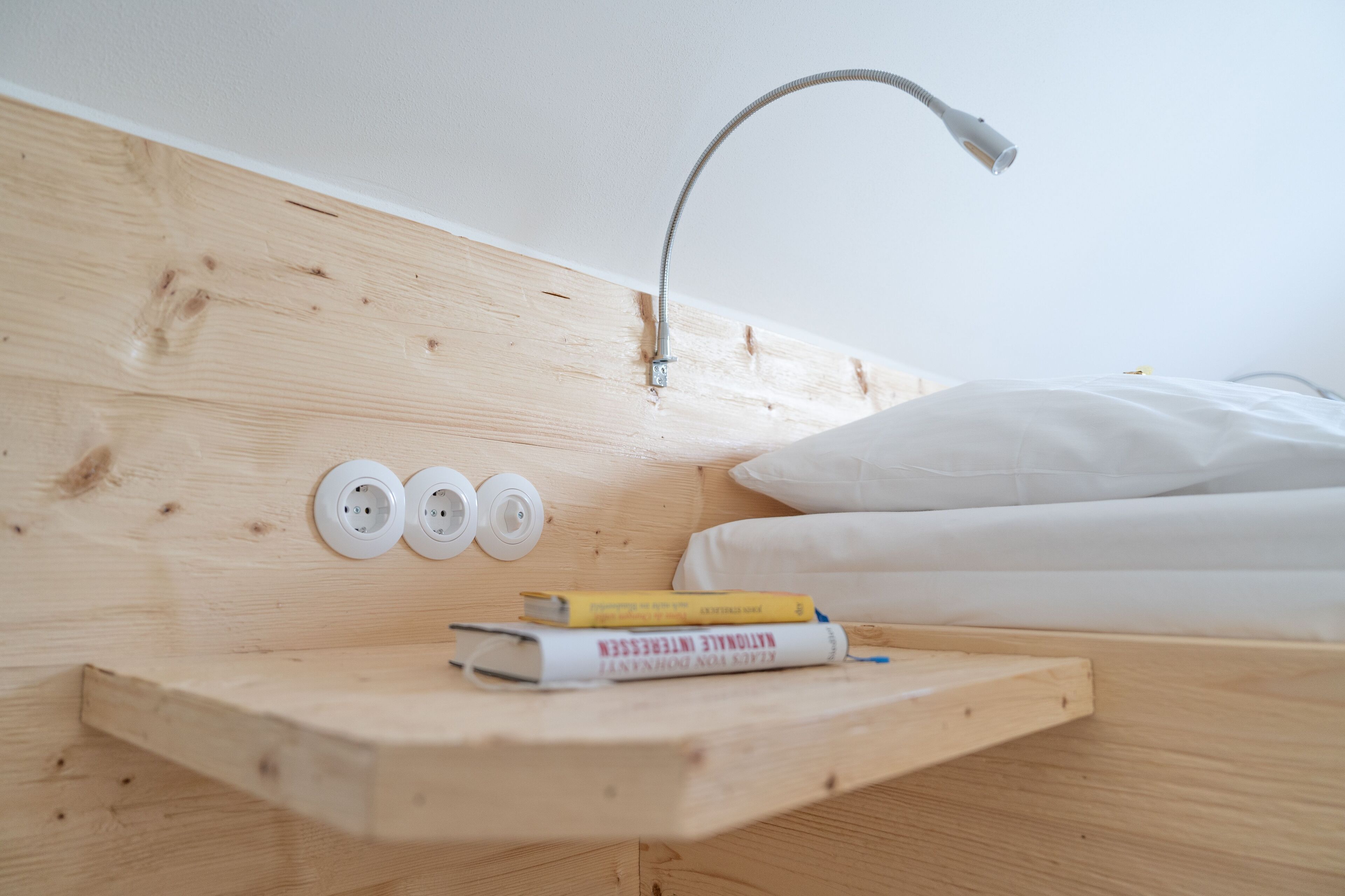 A wooden headboard with a built-in shelf, a white pillow, and a bedside lamp.
