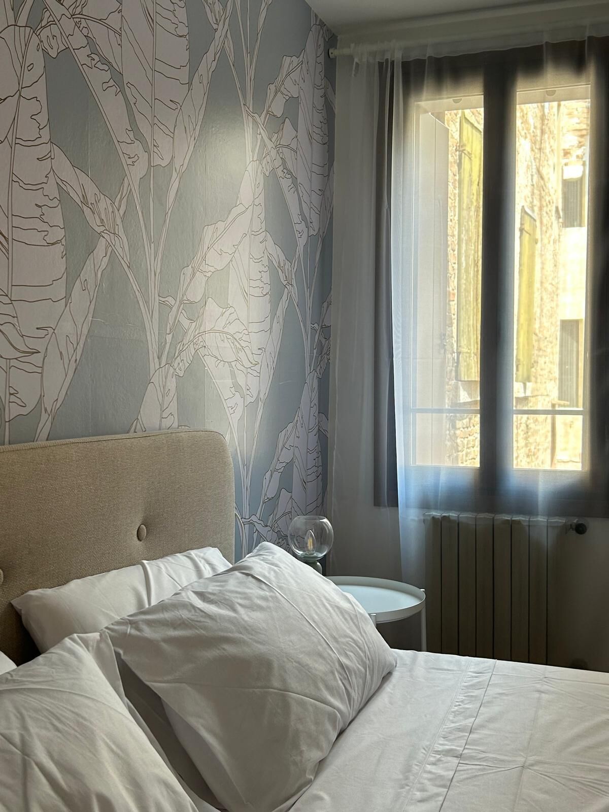Une chambre à coucher avec un lit, une table de chevet sur laquelle se trouve un verre, et une fenêtre avec des rideaux.