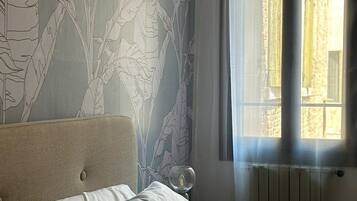 Une chambre à coucher avec un lit, une table de chevet sur laquelle se trouve un verre, et une fenêtre avec des rideaux.
