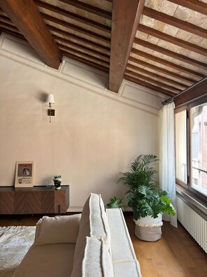 Relax in this serene room with a high ceiling, featuring a comfortable bed, a side table with a lamp, and a potted plant.