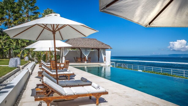 Zona de piscina amb gandules i ombrelles, una cabana i vista a l'oceà.